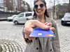 Kvinne holder fram blått bankkort med Mastercard-logo på gate med parkerte biler.