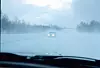Bil med frontlys på snødekt vei i Tromsø, sett gjennom bilrute i vind og snø.