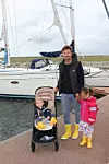 En voksen med to barn ved en seilbåt på en brygge, ett barn i barnevogn.