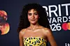 Olivia Dean i gul blomsterkjole foran Brit Awards 2026-vegg i Manchester.