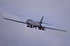 Amerikansk B-1 Lancer-bombefly i lufta med glødende motorer mot grå himmel.