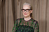 Meryl Streep i sortgrønn mønstret kjole og briller foran beige gardiner i London.