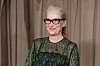 Meryl Streep i sortgrønn mønstret kjole og briller foran beige gardiner i London.
