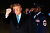 Donald Trump løfter en knyttet neve mens en uniformert militærperson står bak ham.