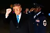 Donald Trump løfter en knyttet neve mens en uniformert militærperson står bak ham.
