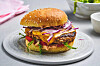 Burger med sesambrød, ost, salat, tomat og rødløk på grå tallerken.