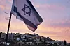 Israelsk flagg vaier over tett bebyggelse i en åsside ved solnedgang.