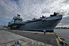 Hangarskipet HMS Prince of Wales ligger ved kai, med en person på kaien foran skipets baug.