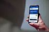 Hånd holder mobiltelefon med nettsiden Slettmeg.no åpen.