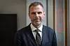 Mann i mørk dress og mønstret slips står innendørs foran en vegg med kunst.