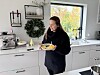 Kvinne holder et fat med mat på et lyst kjøkken med julekrans og vindu.
