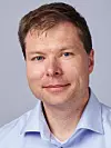 Nærportrett av mann i lyseblå skjorte mot lys grå bakgrunn.