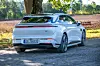 Sølvgrå Porsche Taycan Cross Turismo sett bakfra på grusvei ved et jorde.
