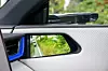 Nærbilde av bildør med blå detalj og sidespeil som reflekterer grønne omgivelser.