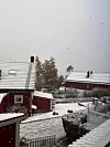 Snø dekker tak, hager og vei mellom røde bolighus i et boligområde.
