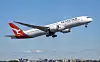 Qantas-passasjerfly med landingshjulene ute flyr lavt over byområde.