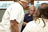Eldre kvinne sitter ved et bord mellom to personer i hvite klær.