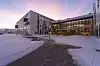 Det nye sykehuset i Hammerfest med opplyst inngangsparti, snø og vei i forgrunnen.