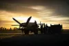Småfly og flere personer i silhuett på bakken ved solnedgang.