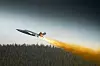 Jetfly flyr over skog med lang ild- og røykstripe bak seg.