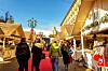 Besøkende går mellom pyntede juleboder langs et rødt teppe i solskinn.