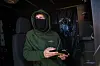 Maskert dronepilot i grønn jakke styrer StarGate med håndkontroll inne i et kjøretøy.