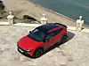 Rød Lamborghini Urus parkert på steinlagt terrasse med strand og hav i bakgrunnen.
