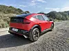 Rød Kia EV6 parkert på grusvei med skog og blå himmel i bakgrunnen.