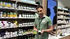 Mann holder to bokser med kosttilskudd foran hyller med vitaminer og helsekost.