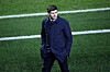 Steven Gerrard i mørk frakk går langs sidelinjen på en fotballbane.