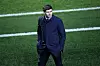 Steven Gerrard i mørk frakk går langs sidelinjen på en fotballbane.