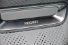 Nærbilde av Recaro-logo på sølvfarget detalj i et perforert bilsete. Recaro-seter med varme, kjøling og massasje kan leveres i flere typer materialer.