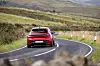 Rød Audi kjører på våt, svingete landevei gjennom grønt åslandskap.