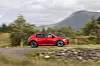 Rød SUV kjører på landevei forbi steinmur, trær og fjell.