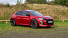 Rød Audi SUV parkert på grusplass foran høyt gress og trær.