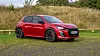Rød Audi SUV parkert på grusplass foran høyt gress og trær.