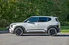 Grå Kia Niro sett fra siden, parkert på asfalt foran tett grønn vegetasjon.