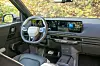 Volvo-førerplass med ratt, digitale skjermer og midtkonsoll, sett mot løvverk utenfor.