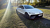 Hvit Hyundai står parkert på gress ved trær, med solstråler fra venstre. Hyundai Ioniq 6 N er helt oppe i toppsjiktet blant seriøse sportsbiler. Hvis du har et snev av fantasi.