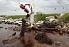 Arbeider i vernedrakt samler oljesøl med absorberende lenser langs en steinete strand.