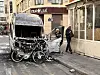 Utbrent varebil med to sykler foran står ved fortauet i en bygateg.