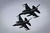 To ukrainske F-16 jagerfly flyr i tett formasjon mot grå himmel.