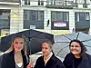 Tre kvinner med paraplyer står foran en bygård i regnvær.