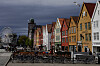 Uteserveringer foran fargerike trehus på Bryggen i Bergen, med tårn og pariserhjul i bakgrunnen.