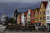 Uteserveringer foran fargerike trehus på Bryggen i Bergen, med tårn og pariserhjul i bakgrunnen.
