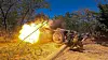 Russisk soldat avfyrer en D-30-haubits i skogsterreng, med flammer fra kanonen.