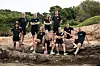 Ti deltakere i svart treningstøy poserer på steiner i et grønt, kupert landskap.