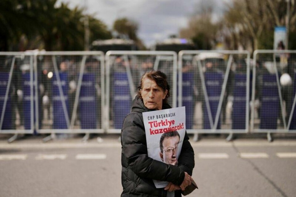 En demonstrant bærer et bilde av Ekrem Imamoglu med slagordet «Tyrkia vinner!» mens hun passerer en politisperring utenfor politistasjonen der han er anholdt.