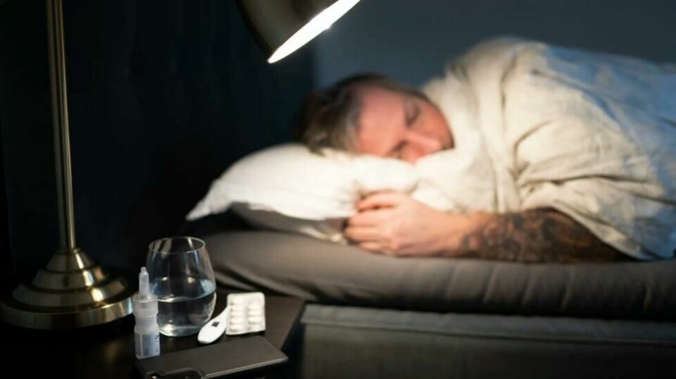 Mann ligger i seng. Vannglass, termometer, piller og nesespray på nattbordet. Norge har hatt høyest sykefravær i Norden hvert år siden 2006, målt i andelen sysselsatte som har vært borte fra jobb i én uke som følge av sykdom.