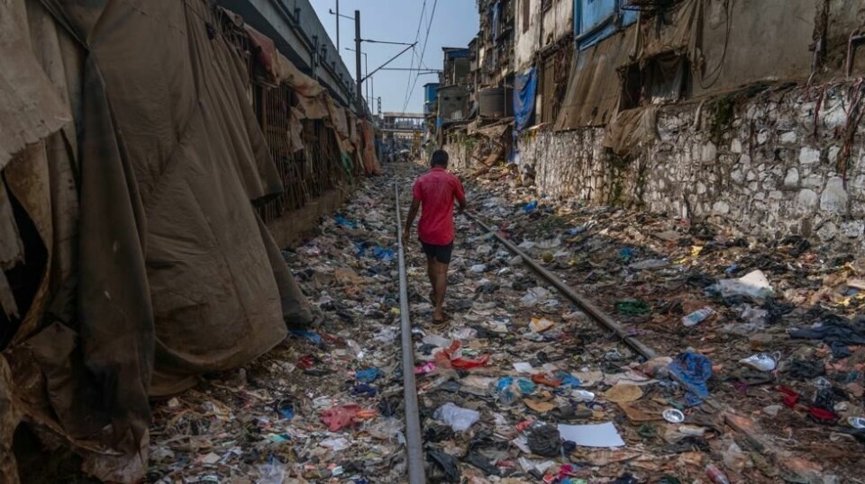 En mann går langs et jernbanespor fylt av plastsøppel i Mumbai i India. Foto: Rafiq Maqbool / AP / NTB